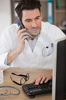 male doctor using mobile phone in clinic against computer