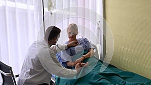 Male doctor using stethoscope on female patient on bed in clinic