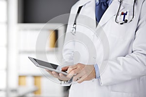 Male doctor using tablet computer in clinic, close-up. Perfect medical service in hospital. Medicine and healthcare