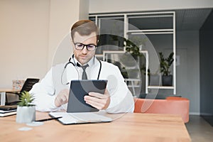 male doctor using tablet computer at his office. General practitioner using digital tablet at his clinic.