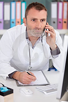 male doctor using telephone while working on computer