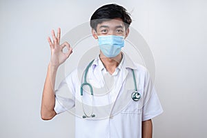 Male doctor wears medical face mask in white coat showing ok hand sign