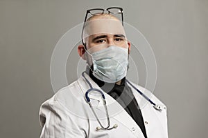 Male doctor in a white coat and mask. Gray background. Close-up. Coronavirus pandemic
