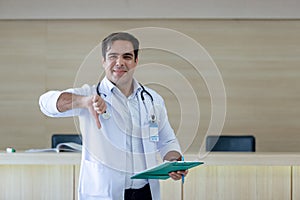 Male doctor white coat show hand thumb down not approved holding folder document standing at counter hospital. doctor checking