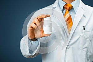 Male Doctor In White Coat With A Stethoscope On Shoulder Holding a Bottle Of Pills Between His Fingers. Healthcare Medical Hospita