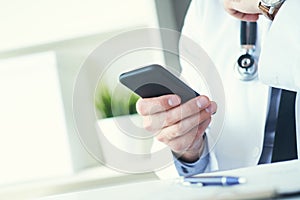 Male doctor in white coat is using a modern smartphone device with touch screen. Doctor hands with mobile phone.