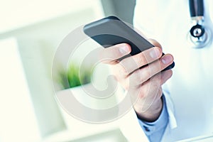 Male doctor in white coat is using a modern smartphone device with touch screen. Doctor hands with mobile phone.