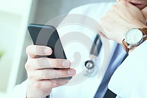 Male doctor in white coat is using a modern smartphone device with touch screen. Doctor hands with mobile phone.