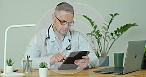 Male doctor in white coat using modern TabletPC device with touch screen. Doctor using DigitalTablet texting to patient