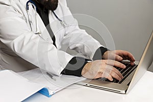 A male doctor in a white coat works in a computer and takes notes. Close-up. Coronavirus pandemic