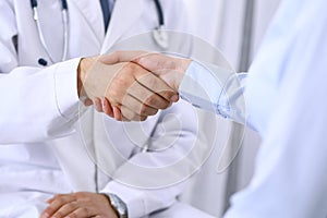 Male doctor and woman patient shaking hands. Partnership in medicine, trust and medical ethics concept