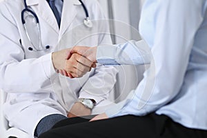 Male doctor and woman patient shaking hands. Partnership in medicine, trust and medical ethics concept