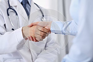 Male doctor and woman patient shaking hands. Partnership in medicine, trust and medical ethics concept