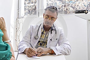 Male doctor is writing prescription to his patient at his medical office