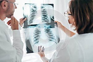 Male doctor and young female colleague examining patient chest x-ray film lungs scan at radiology department in hospital. Covid-19