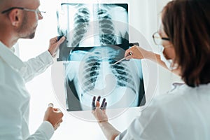 Male doctor and young female colleague examining patient chest x-ray film lungs scan at radiology department in hospital. Covid-19