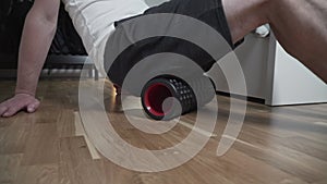 Male doing exercises massage cylinder in small apartment in the bedroom. Young man stretching muscles with yoga roller
