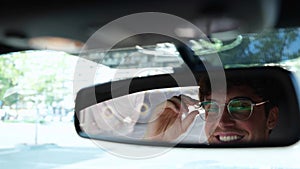 Male driver adjusting his glasses and looking in the rear view mirror while driving in a car in the city. Transport and