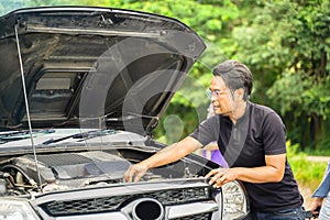 A male driver checks the condition of a car after an accident with an engine on country road side
