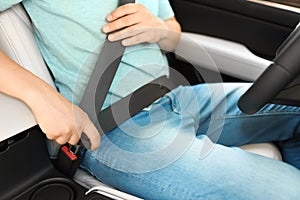 Male driver fastening safety belt in car
