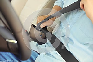 Male driver fastening safety belt in car