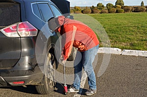 A male driver inflates a car wheel with a mechanical pump.