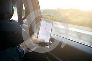 Male driver sitting in the car and holding black mobile smart phone with map gps navigation application