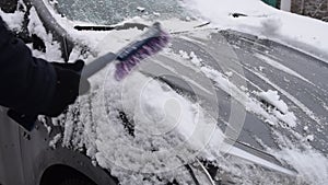 Male driver sweeps snow off car with special brush
