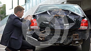 Male driver taking photo of damaged car by smartphone, vehicle insurance proof