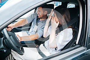 Male driving instructor trying to avoid a collision with another car. Scared young woman covers her face by her hands