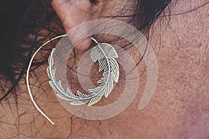 Male ear wearing brass earring in shape of leaf