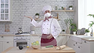 Male elderly chef in a medical mask in a restaurant kitchen