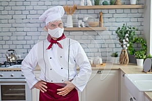 Male elderly chef in a medical mask in a restaurant kitchen