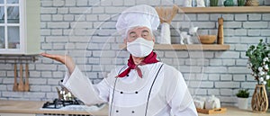 Male elderly chef in a medical mask in a restaurant kitchen