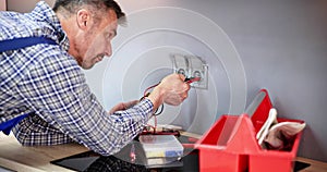 Male Electrician Checking Voltage Of Socket With Multimeter