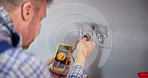 Male Electrician Checking Voltage Of Socket With Multimeter