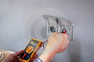 Male electrician checking voltage of socket with multimeter
