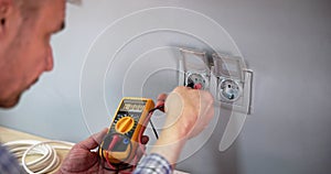 Male Electrician Checking Voltage Of Socket With Multimeter