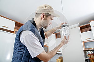 A male electrician fixing light on the ceiling.