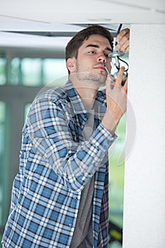 Male electrician fixing light on ceiling with screwdriver