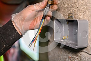 Male electrician holding main power cable ready to be feeded into plug socket on wall
