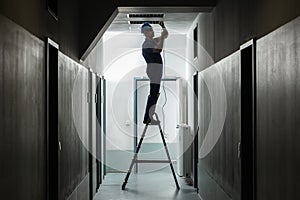 Male Electrician On Step Ladder Installing Light