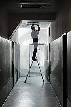 Male Electrician On Step Ladder Installing Light
