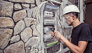 A male electrician works in a switchboard with an electrical con