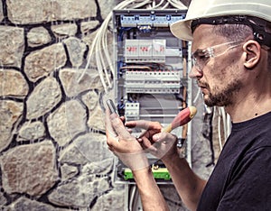 A male electrician works in a switchboard with an electrical con