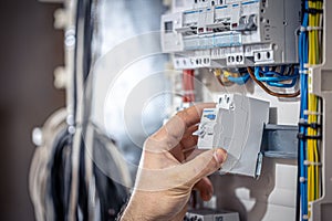 A male electrician works in a switchboard with an electrical connecting cable.