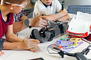 Male electronic engineer with european school children working in smart school lab and testing model of radio controlled