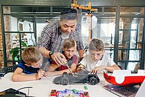 Male electronic engineer with european school children working in smart school lab and testing model of radio controlled