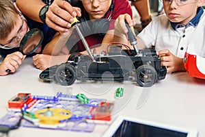 Male electronic engineer with european school children working in smart school lab and testing model of radio controlled