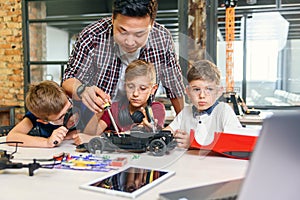 Male electronic engineer with european school children working in smart school lab and testing model of radio controlled